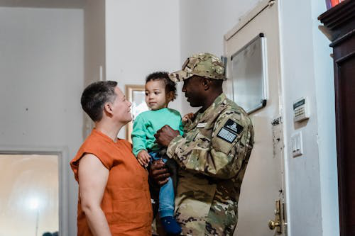 A military father holds his child, discusses with his spouse at home, and symbolizes the family dynamics during a PCS move.